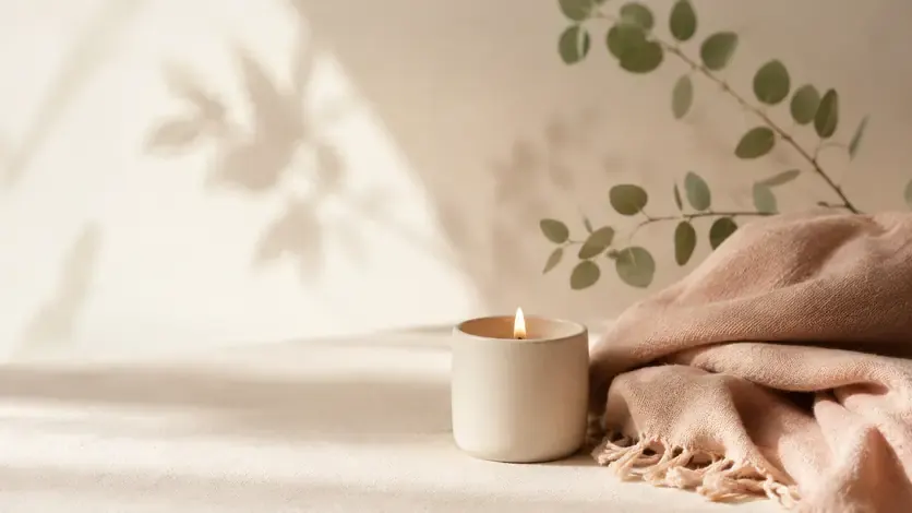 Ruhiges Stillleben – Kerze und weiche Decke in Sage- und Blush-Tönen, viel Weißraum